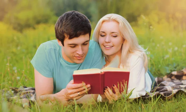 一对快乐的年轻夫妇在夏天的公园里一起躺在绿草上看书 这幅肖像是他们的近照 — 图库照片