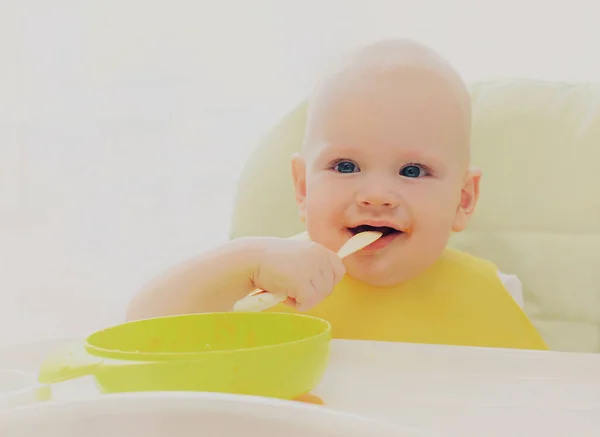 赤ちゃんはスプーンで家のテーブルに座って食べる — ストック写真