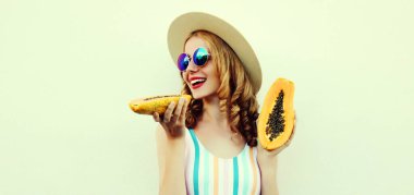 Papayalı mutlu bir genç kadının yaz portresi. Hasır şapka takıyor, beyaz arka planda güneş gözlüğü takıyor.