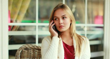 Kafedeki bir masada oturan akıllı telefonlu genç bir kadının portresi.