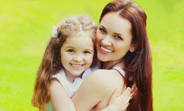 Portrait of beautiful happy smiling mother with little girl child on the grass in a summer park