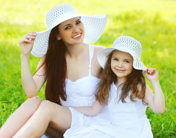 夏の日に草の上にわら帽子をかぶっている小さな女の子の子供と美しい幸せな笑顔の母の肖像画 — ストック写真
