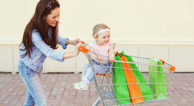 Alışveriş çantaları ve tramvay arabasıyla şehirde yürüyen mutlu anne ve çocuk.