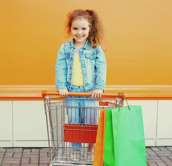城市街道上穿着粗斜纹棉布衣服 手推车和购物袋的小女孩的画像 — 图库照片