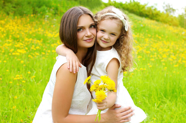 Portrait of beautiful happy smiling mother with little girl child on the grass in a summer park