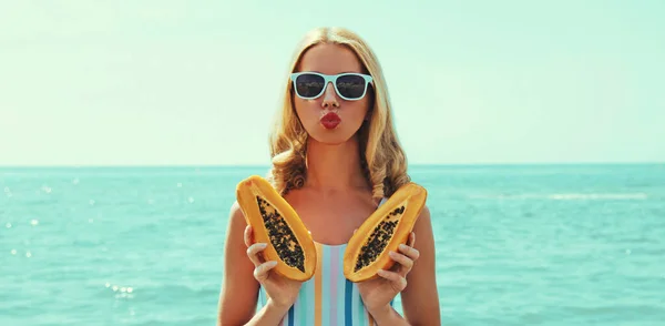 若いです女性の夏の肖像上のビーチとともにPapaya吹いて彼女の唇送信キス上の海の背景 — ストック写真