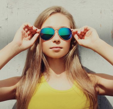 Portrait close up of beautiful blonde young woman wearing a sunglasses posing in a city