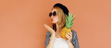 Ananas meyveli güzel bir kadının yaz portresi dudaklarını silip kahverengi bir arka planda hava öpücüğü yolluyor.