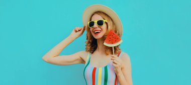 Lolipopu olan mutlu genç bir kadının yaz portresi ya da mavi arka planda hasır şapka takan karpuz şeklinde bir dondurma dilimi.