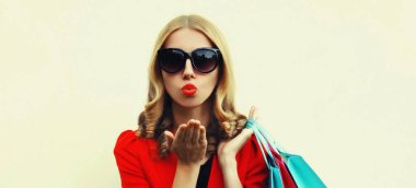 Beyaz tenli, alışveriş torbaları taşıyan, kırmızı dudaklarını silen ve arka planda kırmızı bir iş ceketi giyen genç bir kadının portresi.