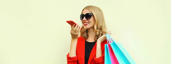 照片中的漂亮微笑的年轻女子背着红色的商务夹克 拿着购物袋用智能手机打电话 — 图库照片