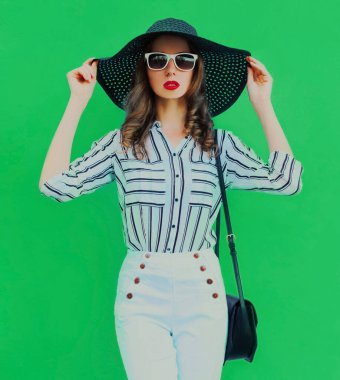 Portrait of beautiful elegant young woman wearing a black round summer hat, white striped shirt on green background