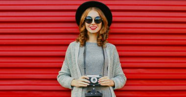 Kırmızı arka planda klasik kameralı genç bir kadın fotoğrafçının portresi.