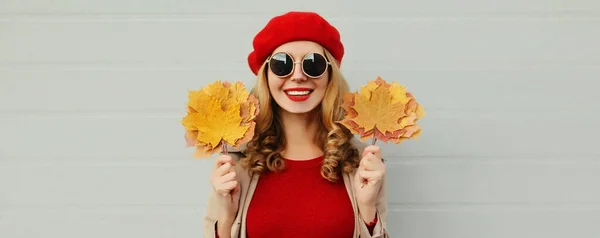 秋の肖像画の美しいです幸せな笑顔若いです女性とともに黄色のカエデの葉身に着けています赤いフランス語ベレー帽上灰色の背景 — ストック写真