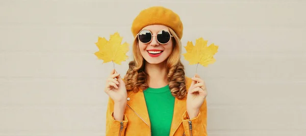 秋の肖像画の美しいです幸せな笑顔若いです女性とともに黄色のカエデの葉身に着けています灰色の背景にフランス語ベレー帽 — ストック写真
