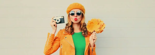 黄色のカエデの葉と灰色の背景にフランス語ベレー帽を身に着けているフィルムカメラと美しい若い女性の秋の肖像画 — ストック写真