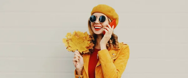 幸せな笑顔若いです女性の秋の肖像黄色のカエデの葉は 灰色の背景にフランス語ベレー帽を身に着けているスマートフォンを呼び出します — ストック写真