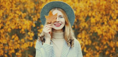 Sarı akçaağaç yapraklı gülen güzel bir kadının sonbahar portresi. Parkta yuvarlak bir şapka takıyor.