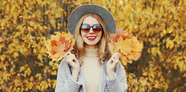 公園で丸い帽子をかぶって黄色のカエデの葉を持つ美しい幸せな笑顔の女性の秋の肖像画 — ストック写真