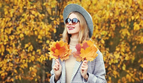 公園で丸い帽子をかぶって黄色のカエデの葉を持つ美しい幸せな笑顔の女性の秋の肖像画 — ストック写真