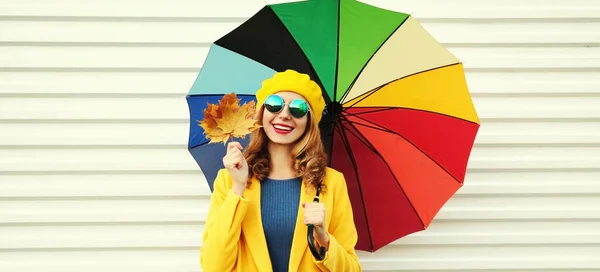 カラフルな傘と黄色のカエデの葉を身に着けている幸せな陽気な笑顔の若い女性の秋の肖像画白い背景にコートとベレー帽 — ストック写真