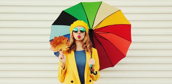 カラフルな傘と黄色のカエデの葉が白い背景にコートとベレー帽を身に着けている幸せな陽気な若い女性の秋の肖像画 — ストック写真