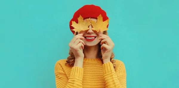 秋の肖像画の幸せな笑顔若いです女性とともに黄色のカエデの葉を身に着けているニットセーター 赤ベレー帽上の青の背景 — ストック写真