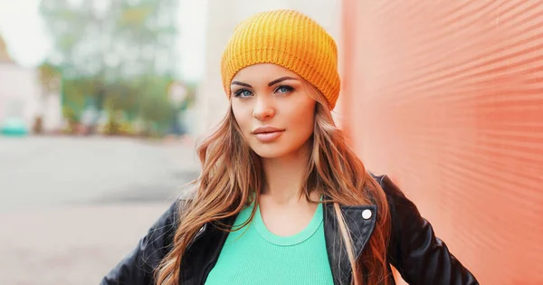 Portrait of beautiful blonde young woman wearing a yellow hat, black rock jacket on red background