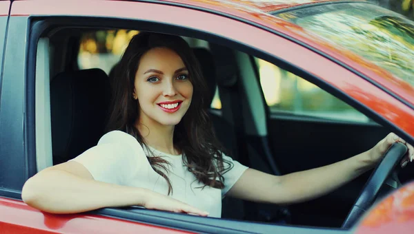 Happy woman driver behind a wheel red car