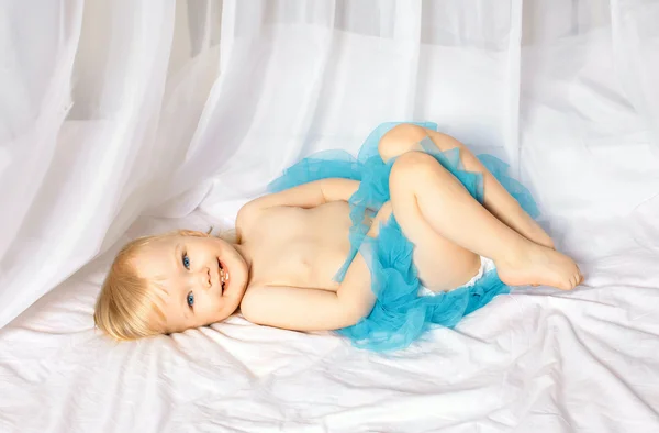 Pequeña linda niña sonriente acostada en una cama en una falda azul —  Fotos de Stock