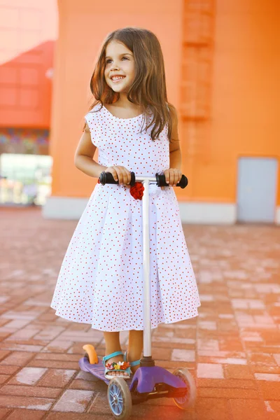 Moda pequena menina alegre no vestido na scooter perto colorido — Fotografia de Stock
