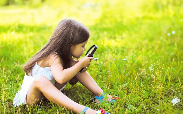 Little girl looking through a magnifying glass on flower — Stock Photo, Image