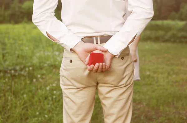 Male hands holding ring in red box, man makes proposal woman — Stock Photo, Image