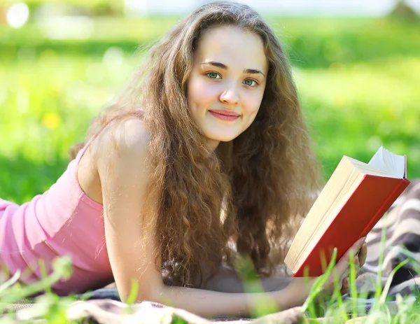 Porträt junges glückliches Mädchen liest ein Buch, das in einem Park in der Sonne liegt — Stockfoto