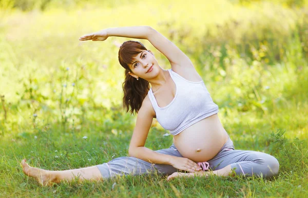 Feliz mulher grávida fazendo exercício na grama — Fotografia de Stock