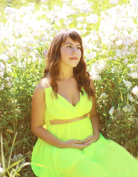 Pregnant lovely woman in flowers in summer sunny day — Stock Photo, Image