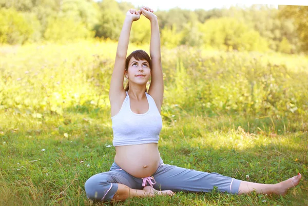 Gravid kvinna gör övning på gräset — Stockfoto