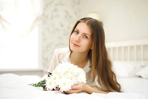 Portrait of a cute young girl on the bed with flowers — Stock Photo, Image