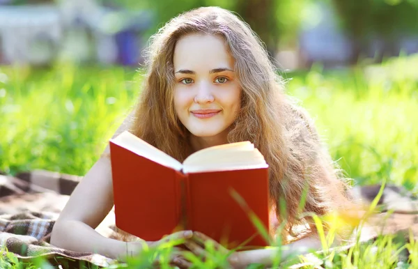 Junges glückliches Mädchen liest ein Buch, das im sonnigen Sommer in einem Park liegt — Stockfoto