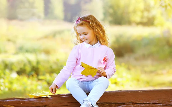 Kleines Mädchen mit gelben Ahornblättern im Herbstpark im Freien — Stockfoto
