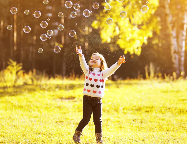 Little child having fun with bubbles soap in sunny autumn day — Stock Photo, Image