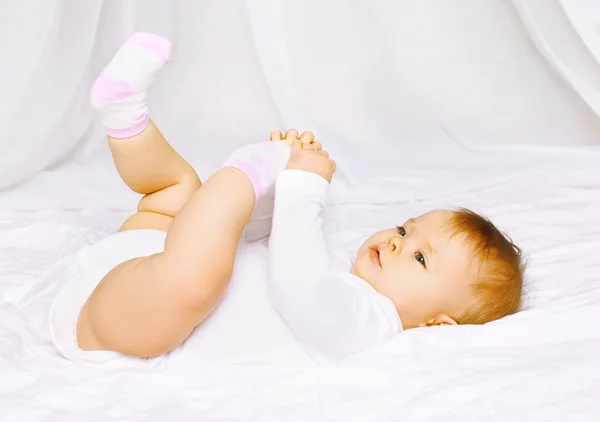 Lindo bebé en calcetines acostado en la cama y sosteniendo las piernas —  Fotos de Stock