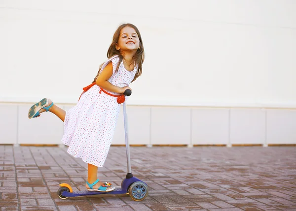 Criança positiva feliz no vestido na scooter na cidade — Fotografia de Stock