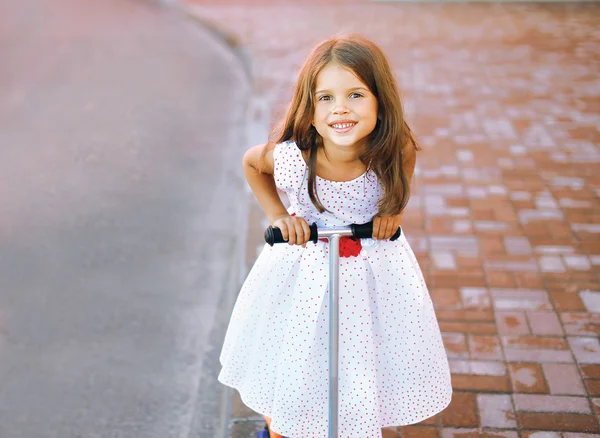 Retrato divertido niña alegre en vestido en el scooter en la c —  Fotos de Stock