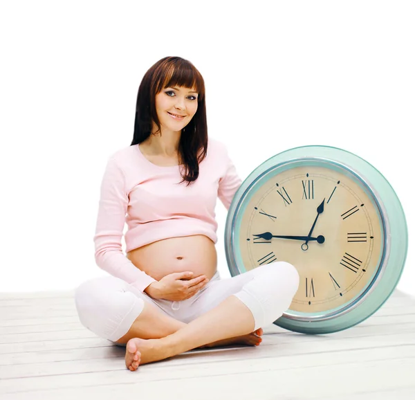 Happy pregnant woman sitting on the floor with a big clock on a — Stock Photo, Image