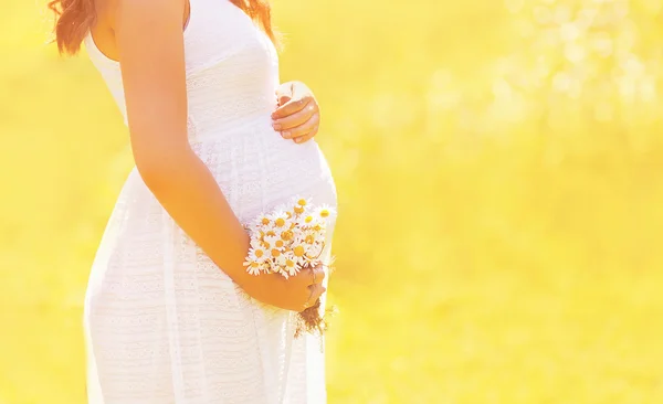 Preciosa mujer embarazada en vestido blanco con flores silvestres en s soleado —  Fotos de Stock