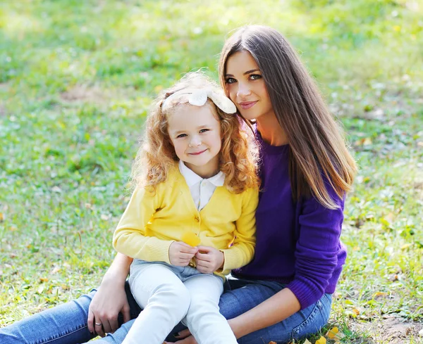 Mother with her daughter sitting on the grass in sunny day — Stock Photo, Image