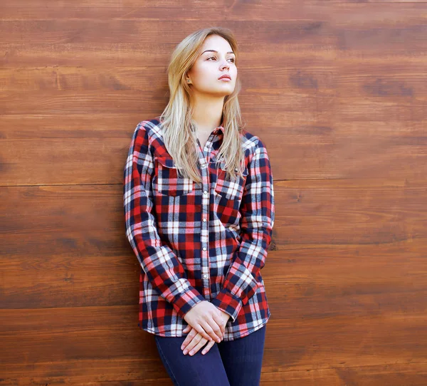 Ragazza hipster in camicia a scacchi posa contro lo schienale in legnogr — Foto Stock