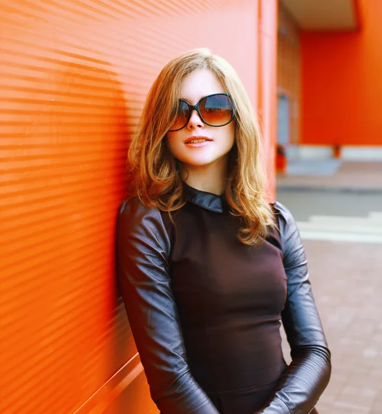 Jolie femme de mode en lunettes de soleil posant contre un mur coloré — Photo