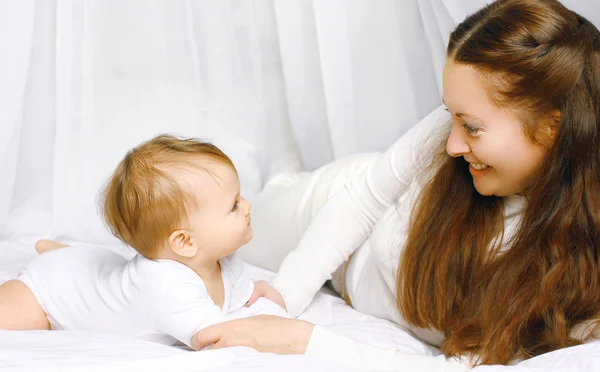 Smiling mother and baby playing in bed home — Stock Photo, Image